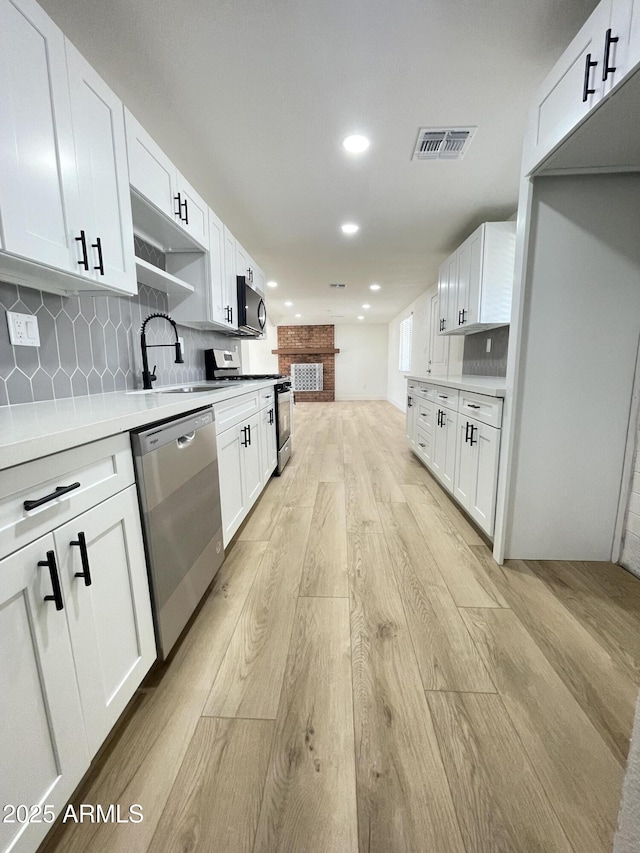 kitchen featuring visible vents, decorative backsplash, appliances with stainless steel finishes, light wood-type flooring, and a sink