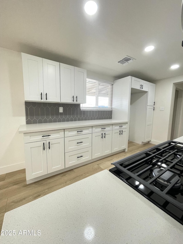 kitchen with light countertops, decorative backsplash, visible vents, and white cabinets