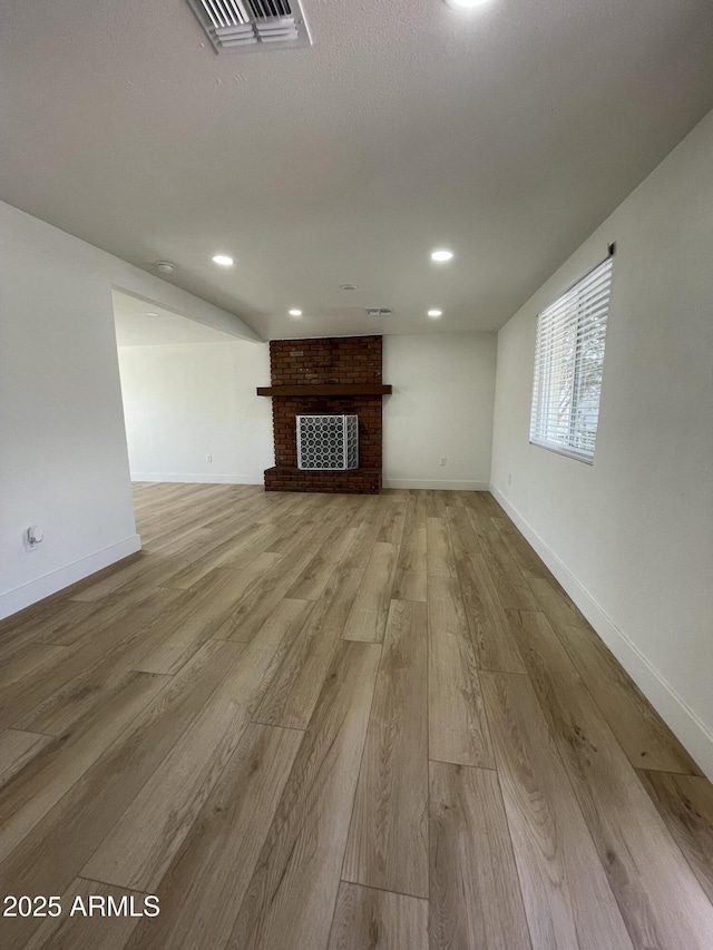 unfurnished living room with recessed lighting, wood finished floors, visible vents, baseboards, and a brick fireplace