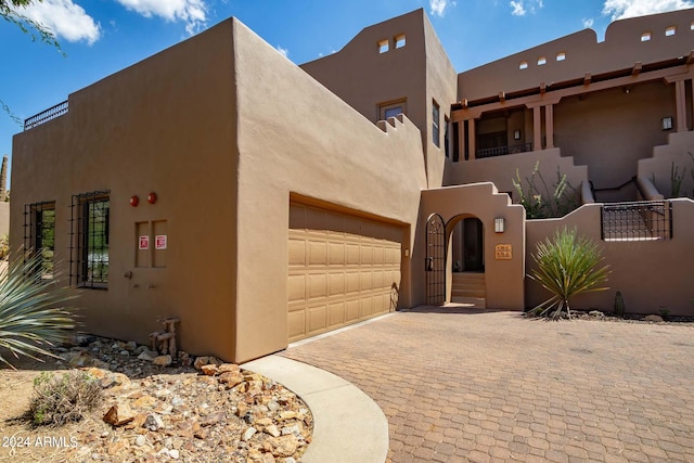 pueblo-style home featuring a garage, decorative driveway, fence, and stucco siding