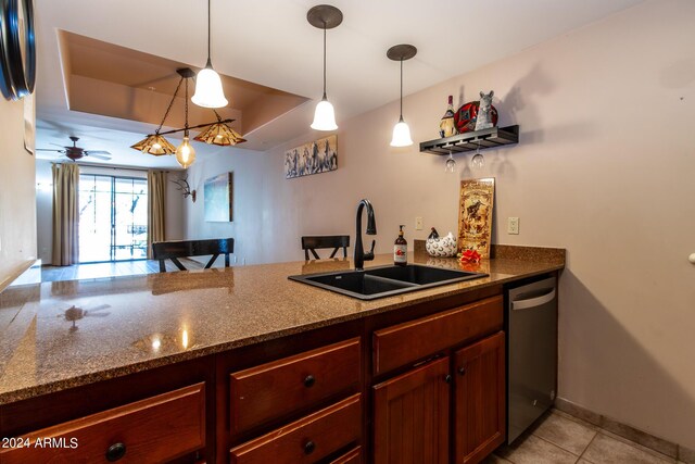 kitchen featuring dark stone counters, sink, stainless steel dishwasher, a raised ceiling, and pendant lighting