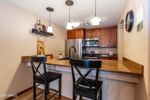 kitchen featuring light hardwood / wood-style flooring, a breakfast bar area, stainless steel appliances, kitchen peninsula, and pendant lighting