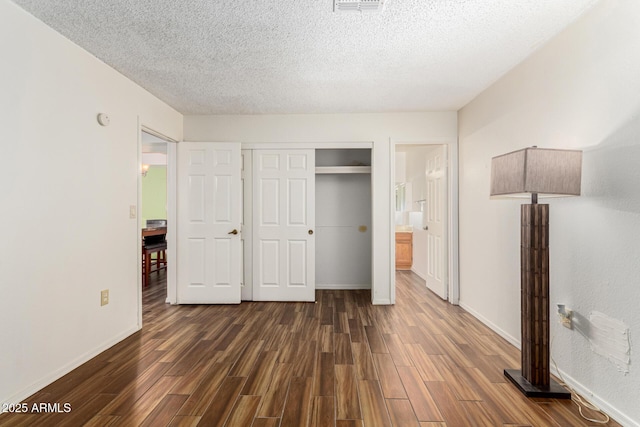 unfurnished bedroom featuring a textured ceiling, a closet, dark hardwood / wood-style flooring, and ensuite bath