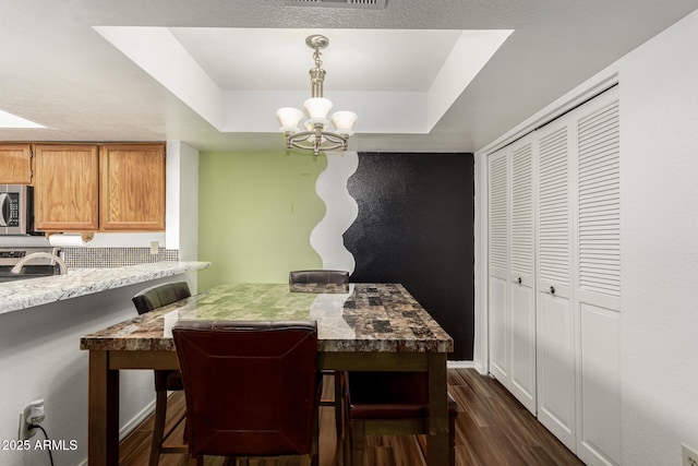 dining room with an inviting chandelier, dark hardwood / wood-style flooring, and a raised ceiling