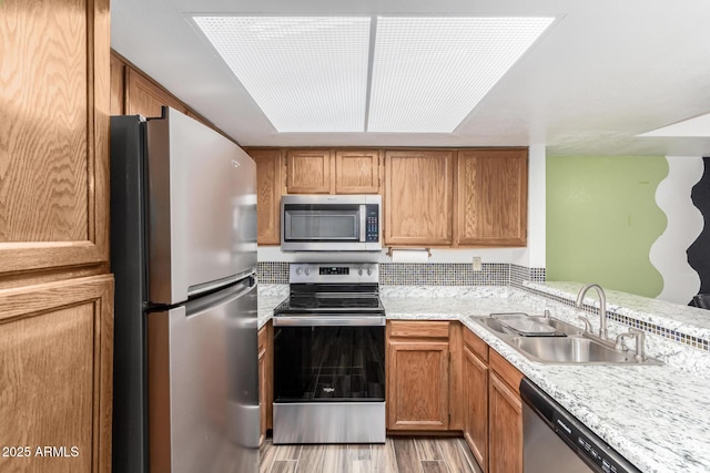 kitchen featuring light stone countertops, appliances with stainless steel finishes, light hardwood / wood-style floors, and sink