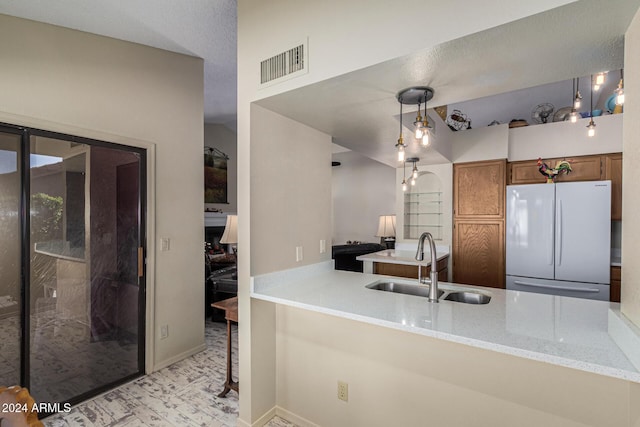 kitchen with light stone countertops, kitchen peninsula, sink, decorative light fixtures, and white fridge