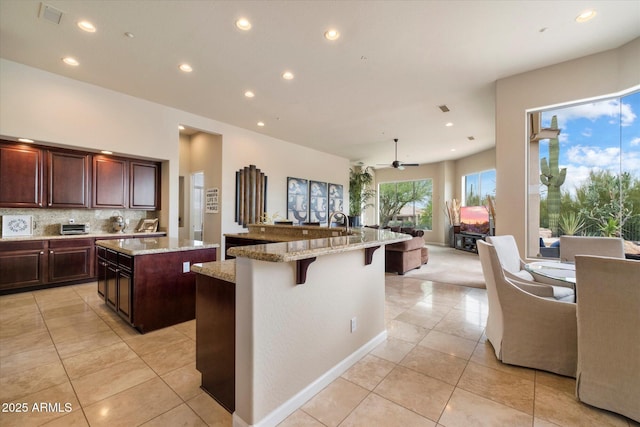 kitchen with a large island with sink, light tile patterned floors, tasteful backsplash, open floor plan, and a breakfast bar area