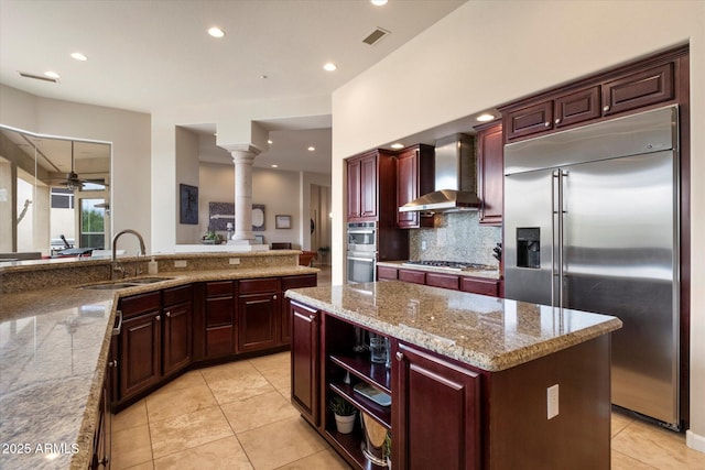 kitchen with wall chimney exhaust hood, stainless steel appliances, a sink, ornate columns, and ceiling fan