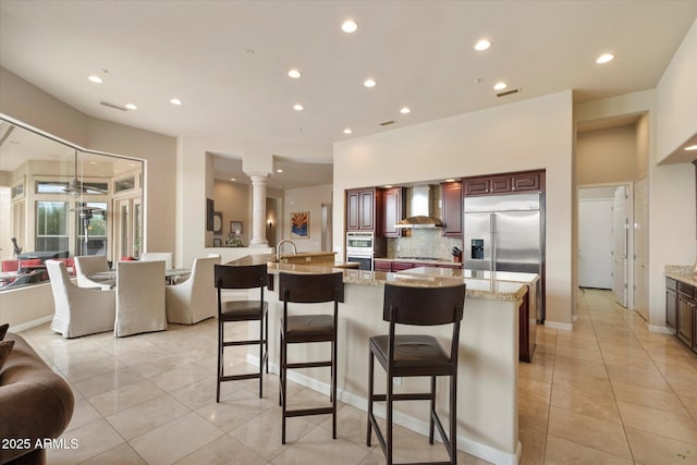 kitchen featuring wall chimney range hood, open floor plan, stainless steel appliances, and light tile patterned floors