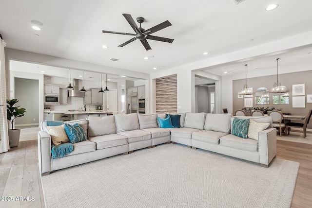 living room featuring recessed lighting, visible vents, ceiling fan with notable chandelier, and light wood-type flooring
