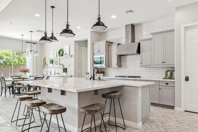 kitchen featuring wall chimney range hood, a sink, visible vents, decorative backsplash, and gray cabinetry