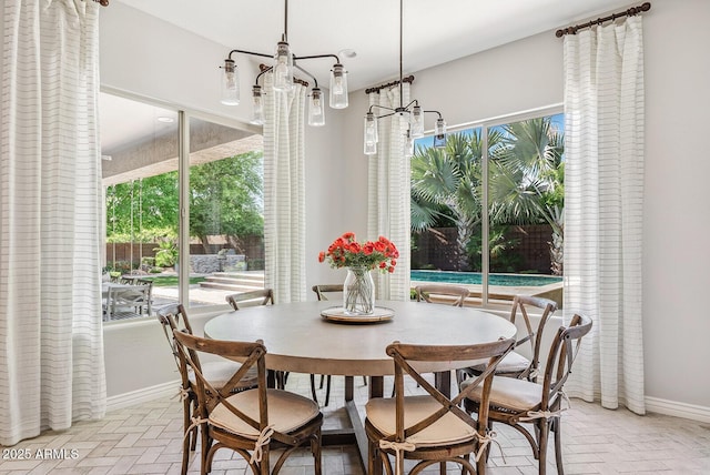 dining area with baseboards, brick floor, a wealth of natural light, and a chandelier