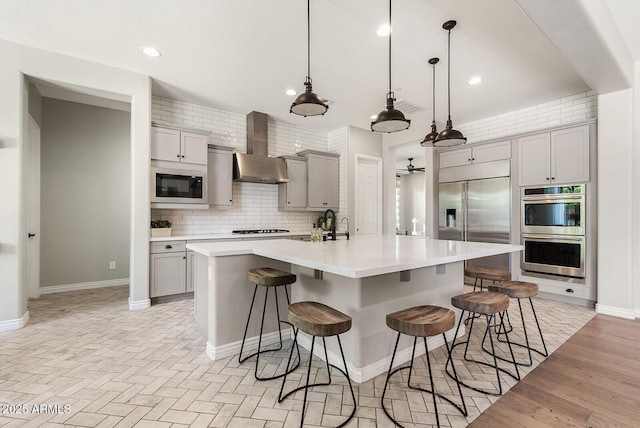 kitchen featuring wall chimney range hood, built in appliances, decorative backsplash, and gray cabinets