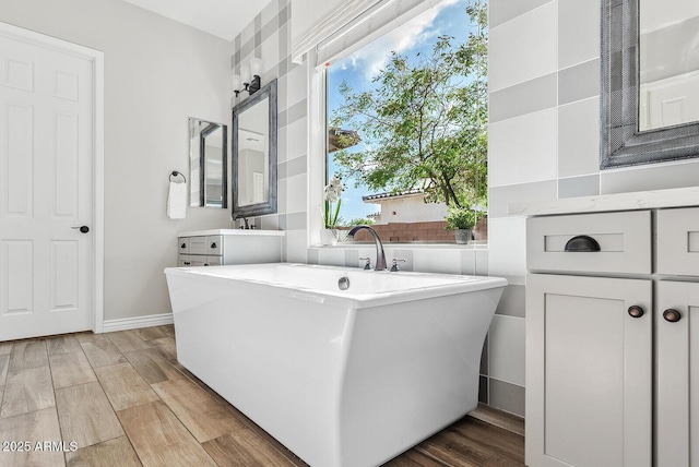 full bathroom with a soaking tub, baseboards, wood finished floors, and vanity