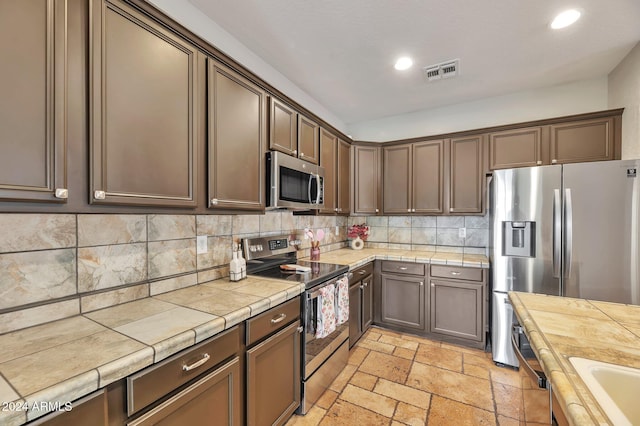 kitchen featuring tasteful backsplash, tile countertops, dark brown cabinetry, and appliances with stainless steel finishes