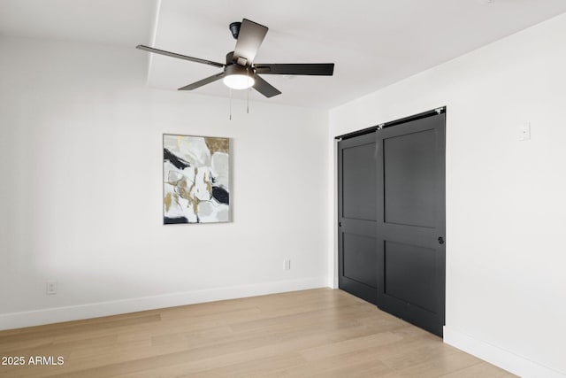 unfurnished bedroom featuring light wood-type flooring, a barn door, baseboards, and ceiling fan