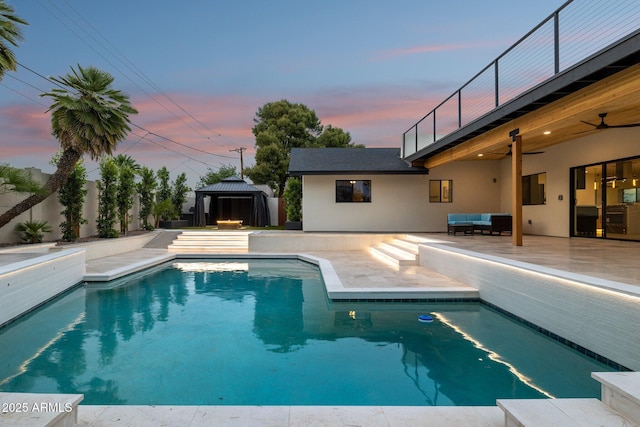 pool at dusk featuring a gazebo, ceiling fan, a patio area, outdoor lounge area, and fence