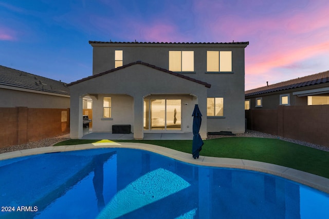 back house at dusk featuring a fenced in pool