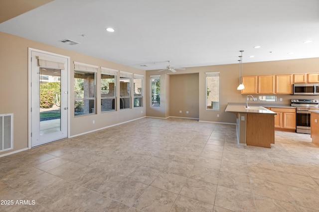 kitchen with sink, decorative light fixtures, light brown cabinets, appliances with stainless steel finishes, and a kitchen island with sink