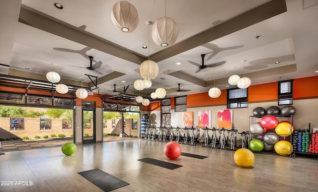 gym with wood-type flooring, a raised ceiling, and ceiling fan