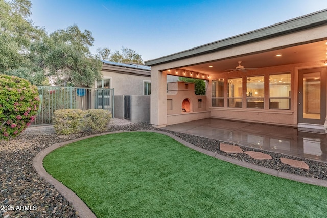 back of property with ceiling fan, a lawn, exterior fireplace, and a patio area