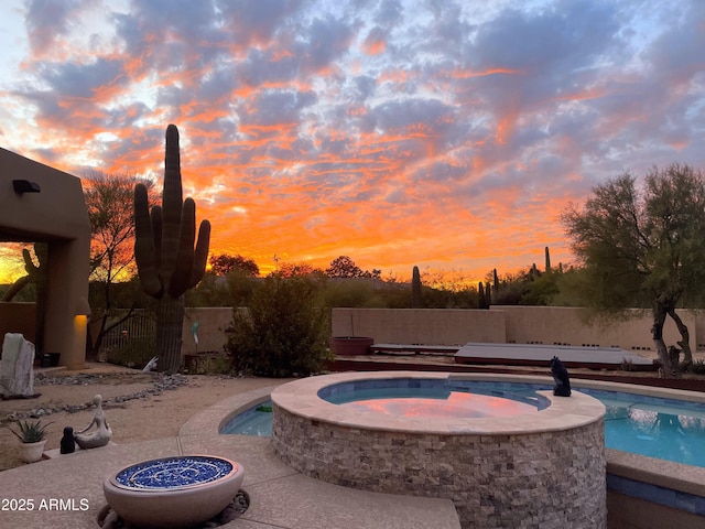 pool at dusk featuring a fenced in pool, an in ground hot tub, and a fenced backyard