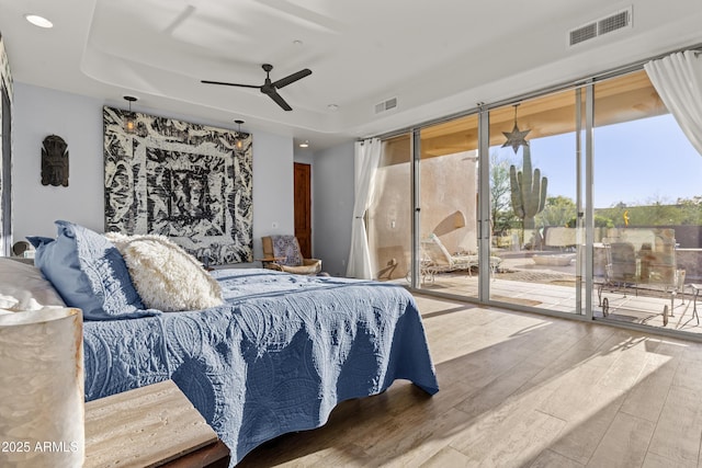 bedroom featuring access to outside, a tray ceiling, wood finished floors, and visible vents