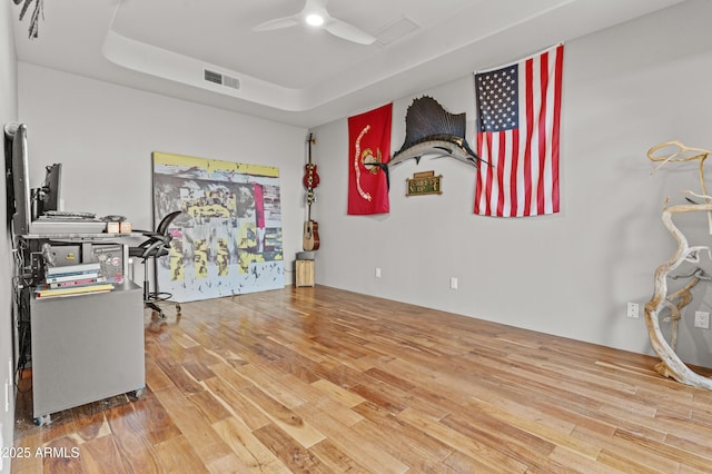 interior space with a ceiling fan, a tray ceiling, visible vents, and wood finished floors