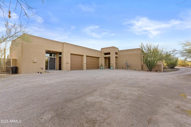 pueblo revival-style home with an attached garage, driveway, and stucco siding