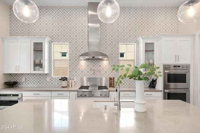 kitchen with decorative light fixtures, white cabinetry, double oven, and wall chimney exhaust hood