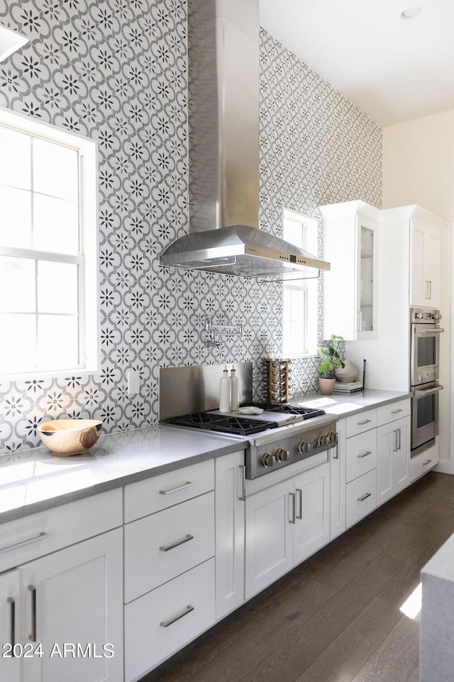 kitchen featuring white cabinetry, wall chimney range hood, dark hardwood / wood-style flooring, backsplash, and appliances with stainless steel finishes