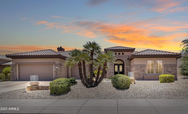 mediterranean / spanish house with stucco siding, concrete driveway, a garage, stone siding, and a tiled roof