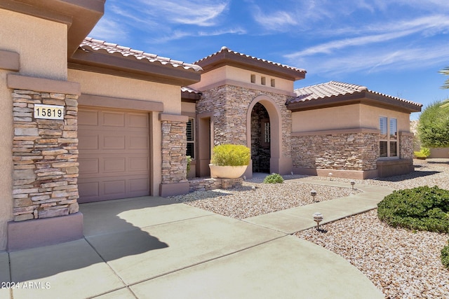 view of front of house with an attached garage, stone siding, a tile roof, and stucco siding