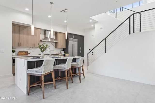 kitchen featuring visible vents, a center island with sink, built in fridge, light countertops, and wall chimney exhaust hood