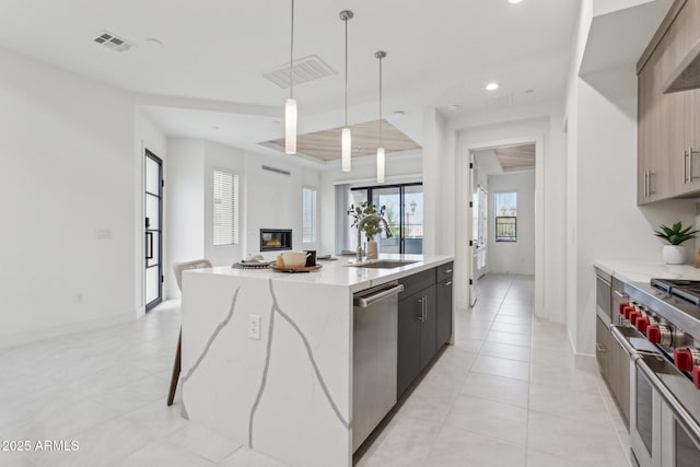 kitchen featuring appliances with stainless steel finishes, a sink, a kitchen island with sink, light tile patterned floors, and visible vents