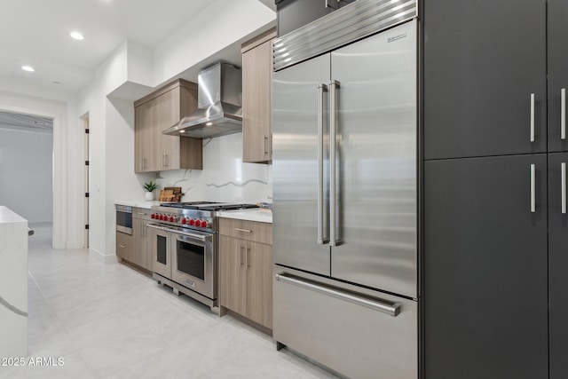 kitchen featuring wall chimney range hood, recessed lighting, light countertops, light tile patterned floors, and premium appliances