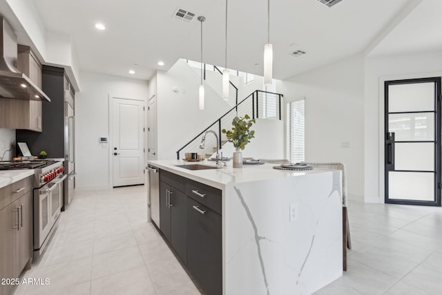 kitchen featuring appliances with stainless steel finishes, modern cabinets, a sink, wall chimney exhaust hood, and an island with sink