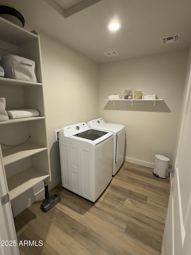 clothes washing area featuring visible vents, separate washer and dryer, wood finished floors, laundry area, and baseboards