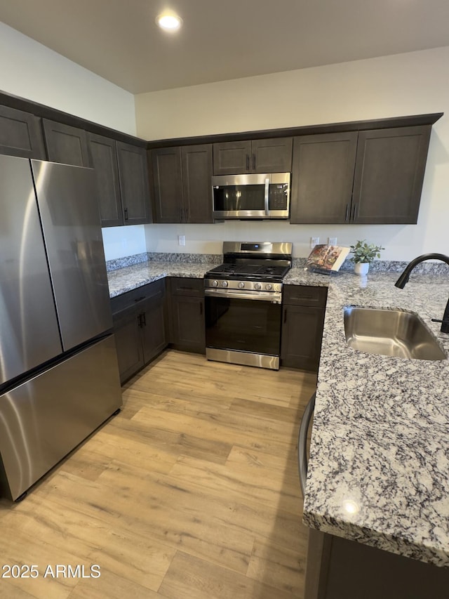 kitchen featuring light stone counters, a sink, light wood-style floors, dark brown cabinets, and appliances with stainless steel finishes