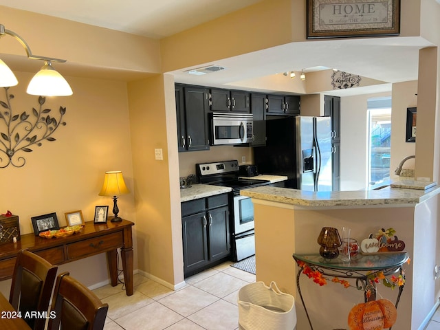 kitchen featuring stainless steel appliances, kitchen peninsula, light stone counters, light tile patterned floors, and hanging light fixtures