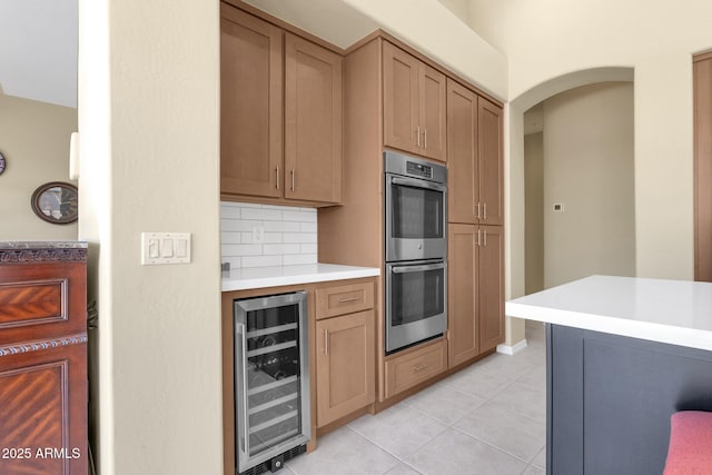 kitchen featuring wine cooler, double oven, light countertops, tasteful backsplash, and light tile patterned floors