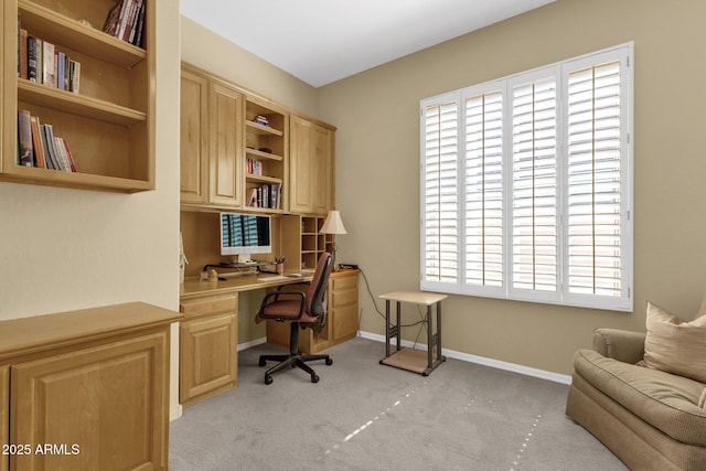 office space with baseboards, plenty of natural light, built in desk, and light carpet