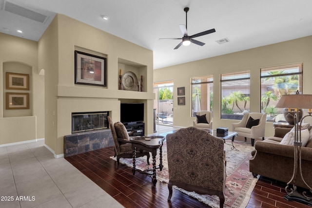 living area with a glass covered fireplace, wood finish floors, a ceiling fan, and visible vents
