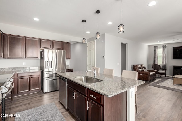 kitchen featuring sink, a breakfast bar area, stainless steel appliances, a center island with sink, and decorative light fixtures