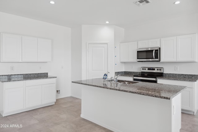 kitchen featuring white cabinetry, sink, dark stone counters, a center island with sink, and appliances with stainless steel finishes