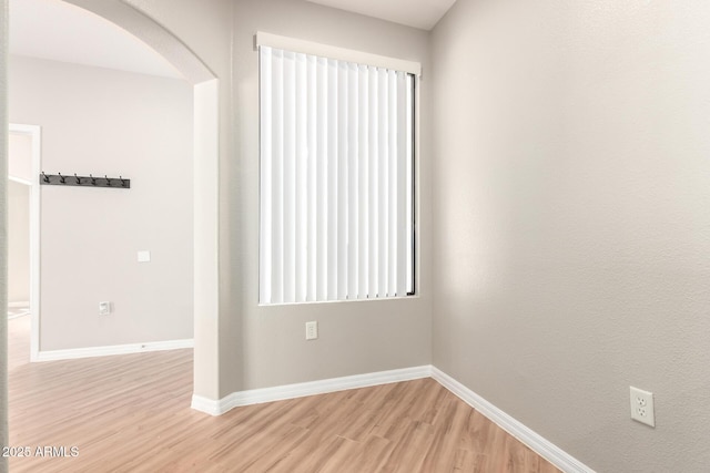 unfurnished room featuring baseboards, arched walkways, and light wood-type flooring