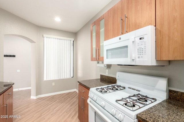 kitchen featuring white appliances, baseboards, light wood finished floors, arched walkways, and glass insert cabinets