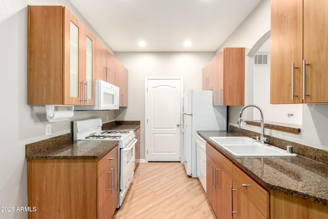 kitchen with visible vents, glass insert cabinets, light wood-style floors, white appliances, and a sink