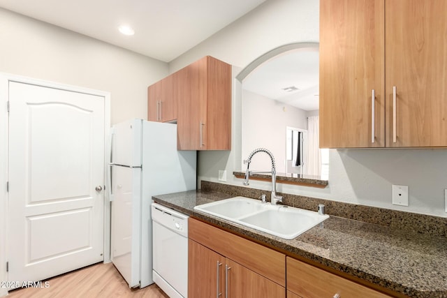 kitchen featuring visible vents, a sink, dark stone countertops, arched walkways, and dishwasher