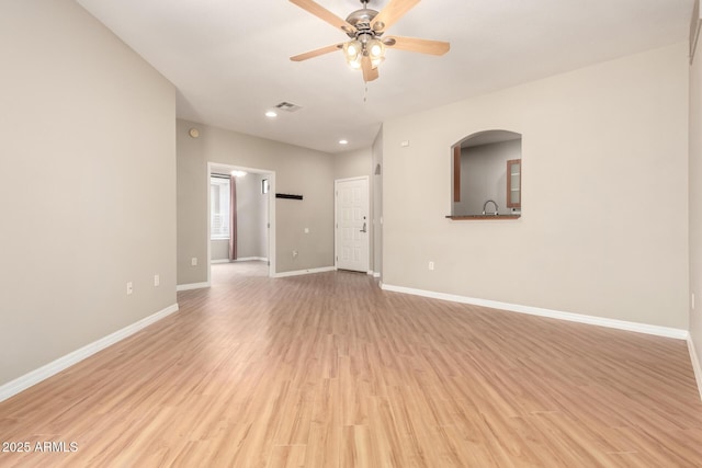 unfurnished living room with light wood-type flooring, visible vents, a sink, baseboards, and ceiling fan